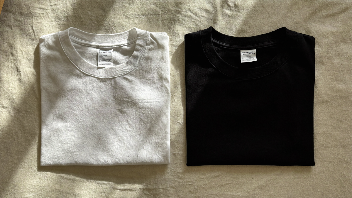 Two plain cotton T-shirts, one white and one black, folded side by side on a linen surface