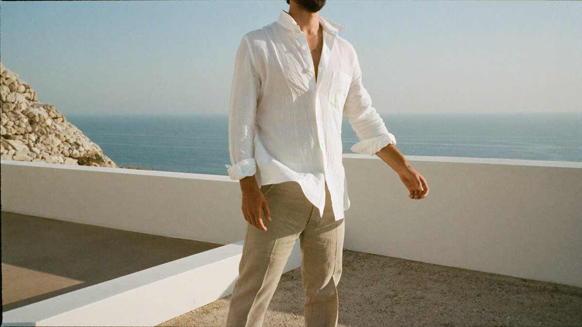 A man in a white linen shirt and natural linen trousers on a sunlit Mediterranean terrace